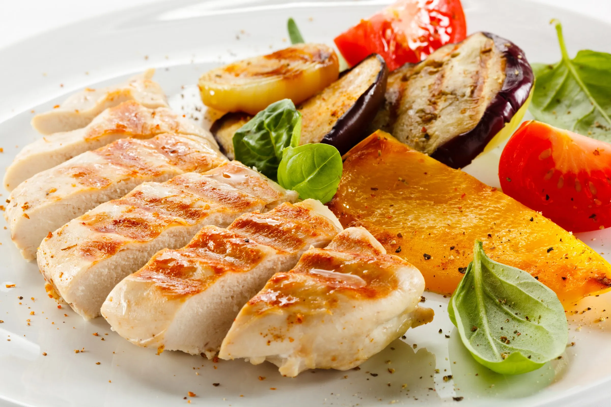 Piatto di petto di pollo alla griglia con verdure grigliate, pomodorini e basilico fresco
