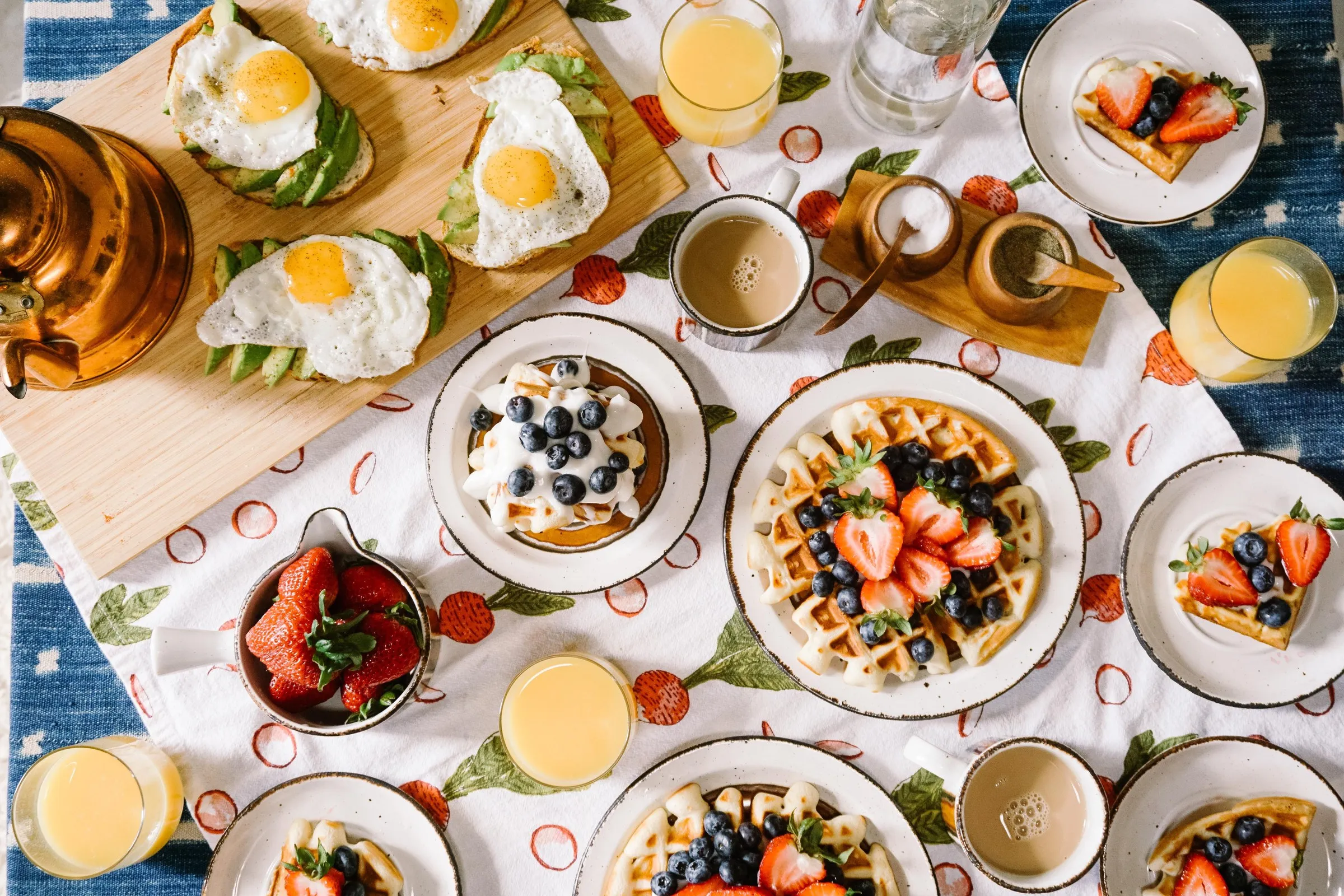 Tavola apparecchiata per la colazione vista dall'alto, con frutta fresca, uova, avocado toast e succo d'arancia